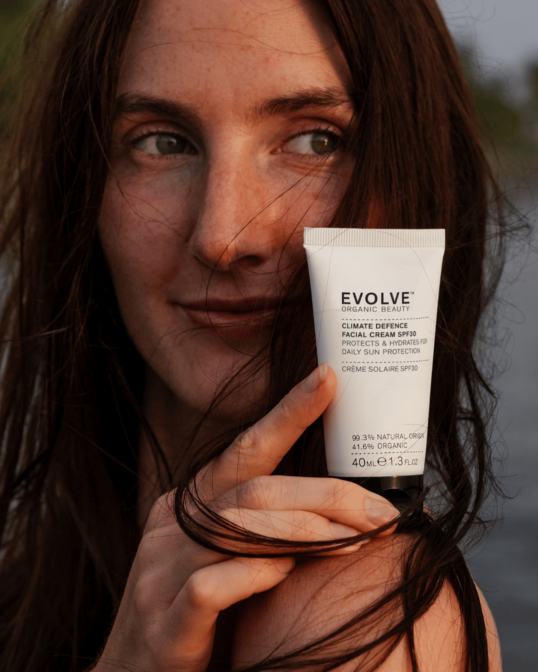Person holding a tube of Evolve skincare product with a blurred background