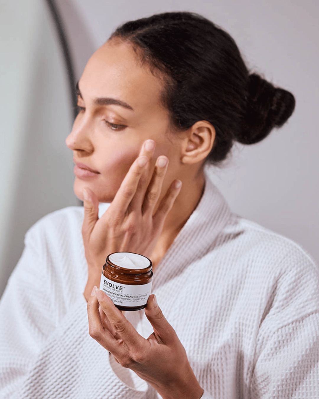 Woman applying cream to her face with a jar of Evolve cream in her hand.