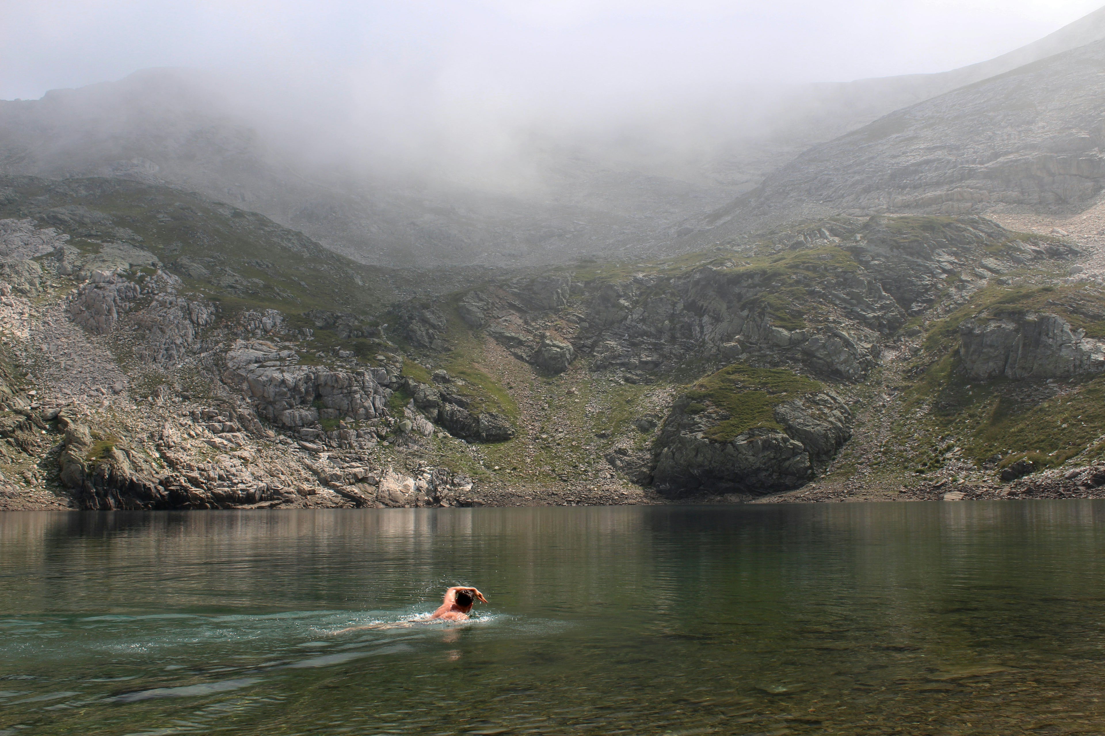 Person swimming in a lake surrounded by misty mountains